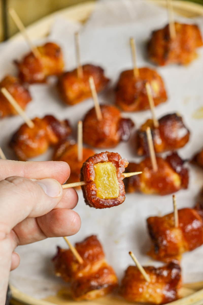 Bacon wrapped pineapple bites on platter with one upclose