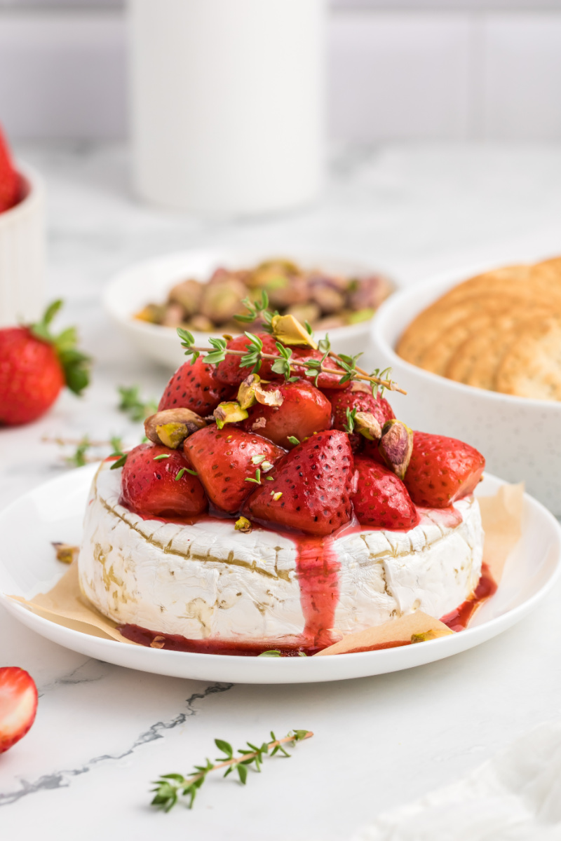 Wheel of baked brie with strawberries on top shown on serving table